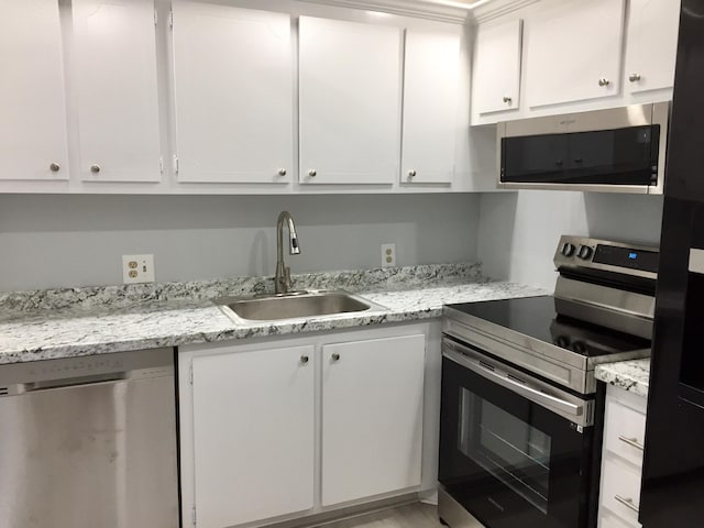 kitchen with sink, stainless steel appliances, light stone counters, and white cabinetry