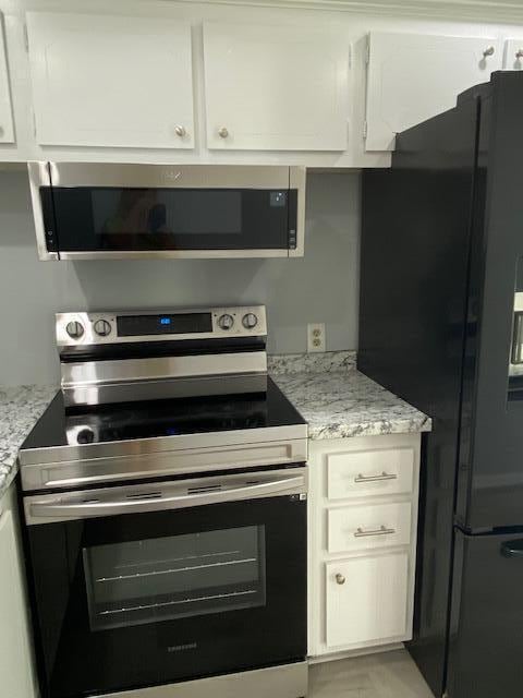 kitchen with white cabinetry, light stone counters, and appliances with stainless steel finishes