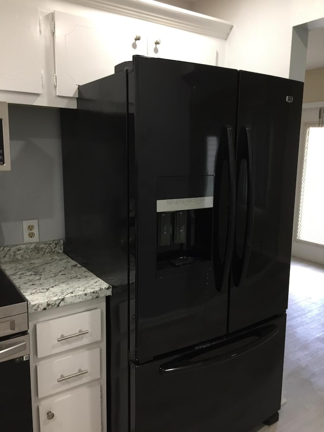 kitchen with black fridge, white cabinetry, light wood-style floors, and light stone countertops