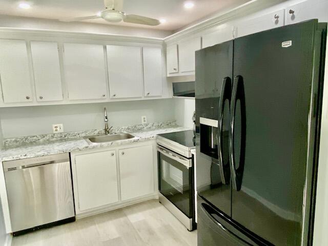 kitchen with light wood finished floors, a sink, ceiling fan, stainless steel appliances, and white cabinetry