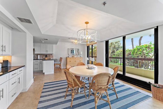 dining space with a raised ceiling, a chandelier, and light tile patterned flooring