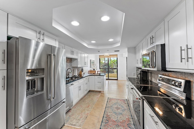 kitchen with stainless steel appliances, white cabinetry, a tray ceiling, light tile patterned flooring, and decorative backsplash