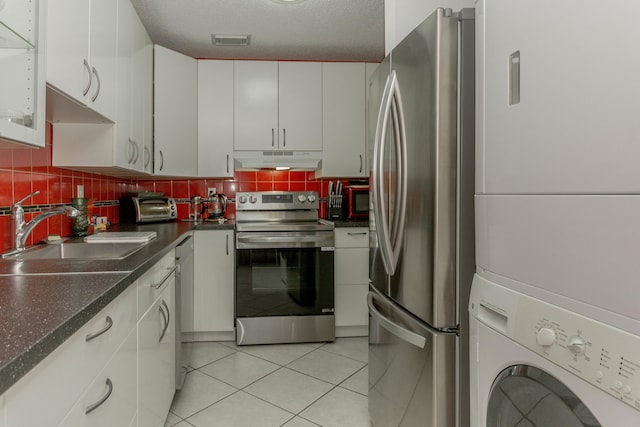 kitchen featuring decorative backsplash, appliances with stainless steel finishes, sink, stacked washer and clothes dryer, and white cabinetry