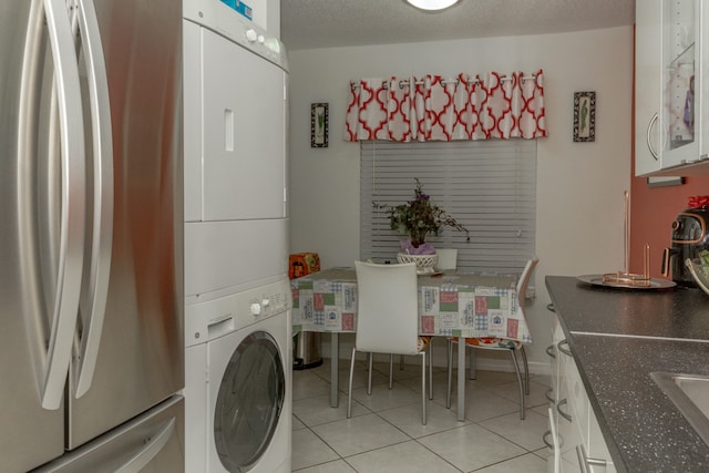 laundry room with sink, light tile patterned floors, a textured ceiling, and stacked washer and clothes dryer