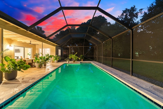 pool at dusk featuring a bar, glass enclosure, ceiling fan, and a patio area