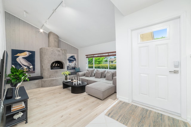 living room with wood walls, a fireplace, rail lighting, and high vaulted ceiling