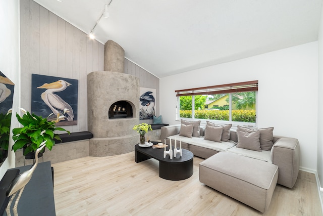 living room with a premium fireplace, rail lighting, wood-type flooring, and vaulted ceiling