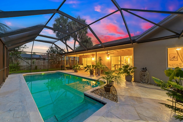 pool at dusk with a lanai, ceiling fan, and a patio