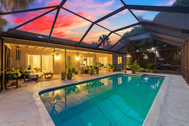 pool at dusk featuring a patio area, ceiling fan, outdoor lounge area, and glass enclosure