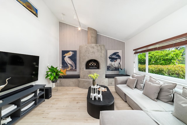 living room with rail lighting, vaulted ceiling, a premium fireplace, light hardwood / wood-style floors, and wood walls