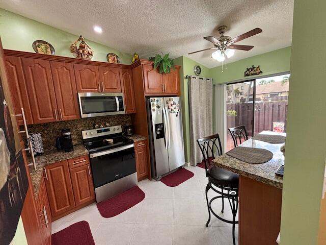 kitchen featuring a textured ceiling, stainless steel appliances, lofted ceiling, ceiling fan, and dark stone counters