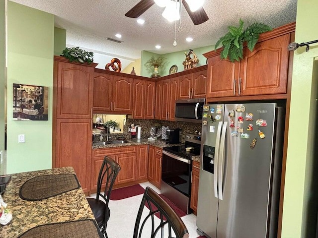 kitchen with a textured ceiling, appliances with stainless steel finishes, sink, ceiling fan, and dark stone counters