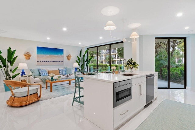 kitchen featuring floor to ceiling windows, stainless steel microwave, sink, an island with sink, and white cabinets