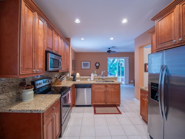 kitchen with appliances with stainless steel finishes, light stone counters, sink, kitchen peninsula, and ceiling fan