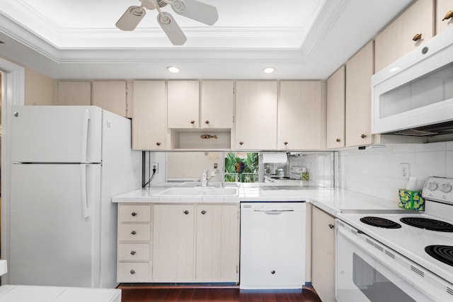 kitchen with white appliances, a sink, a tray ceiling, ornamental molding, and cream cabinetry