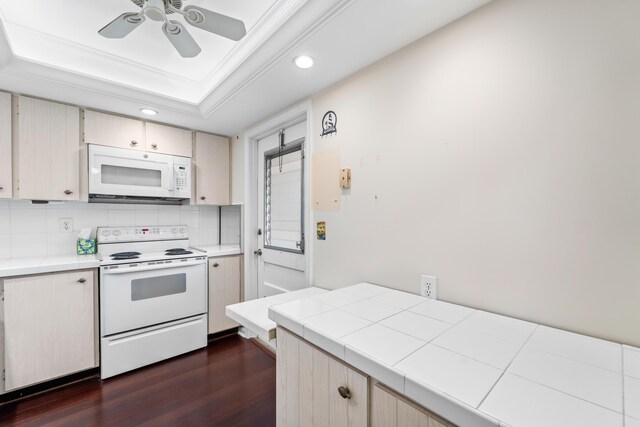 kitchen featuring white appliances, dark hardwood / wood-style flooring, a tray ceiling, ornamental molding, and ceiling fan