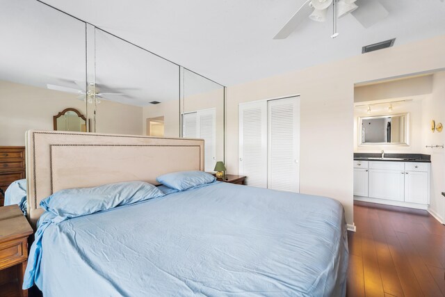 bedroom featuring ceiling fan, dark hardwood / wood-style floors, sink, and multiple closets