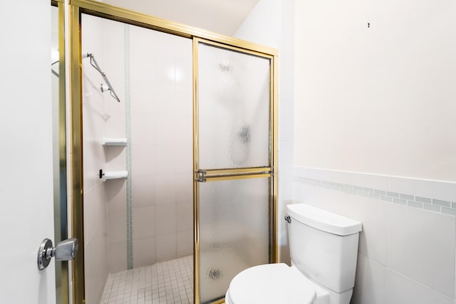 bathroom featuring tile walls, toilet, and a shower with door