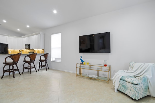 kitchen featuring kitchen peninsula, a kitchen breakfast bar, refrigerator, vaulted ceiling, and white cabinets