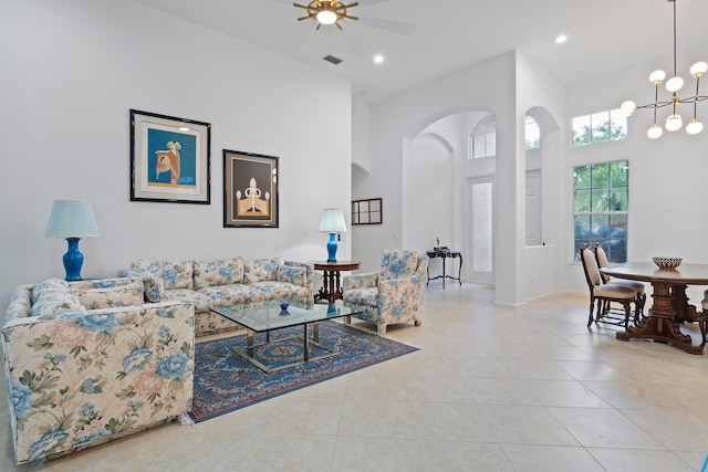 living room with ceiling fan with notable chandelier, a towering ceiling, and light tile patterned floors