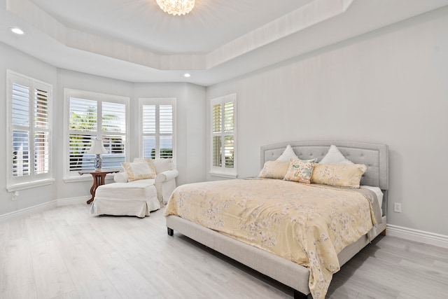 bedroom with a raised ceiling, an inviting chandelier, and hardwood / wood-style flooring