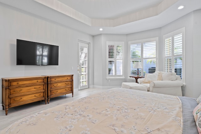 bedroom featuring access to exterior, a tray ceiling, and light hardwood / wood-style flooring