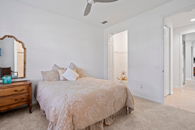 bedroom with ceiling fan, light colored carpet, a walk in closet, and a closet