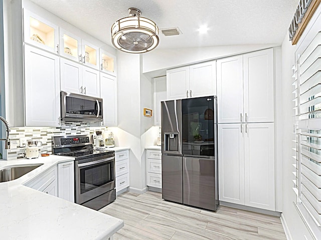 kitchen featuring stainless steel appliances, light stone counters, vaulted ceiling, and white cabinetry