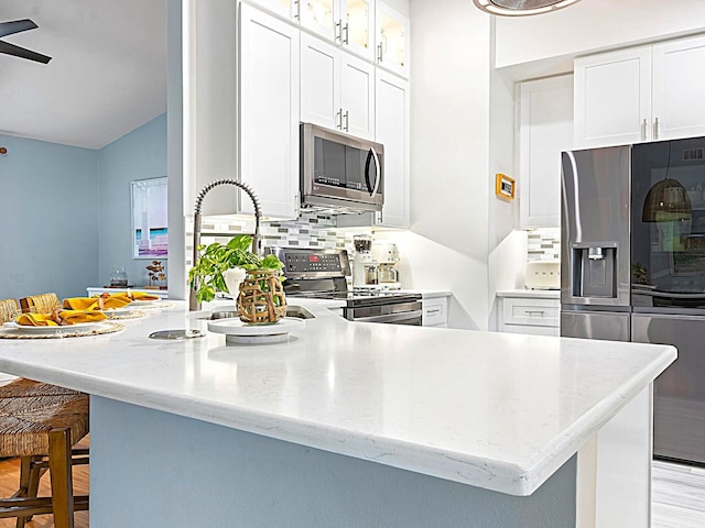 kitchen with a kitchen bar, stainless steel appliances, ceiling fan, and white cabinetry