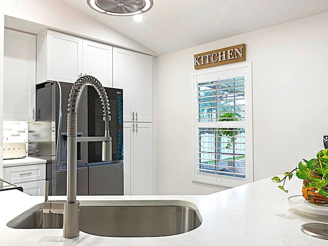 kitchen with a textured ceiling, vaulted ceiling, sink, white cabinetry, and light stone counters