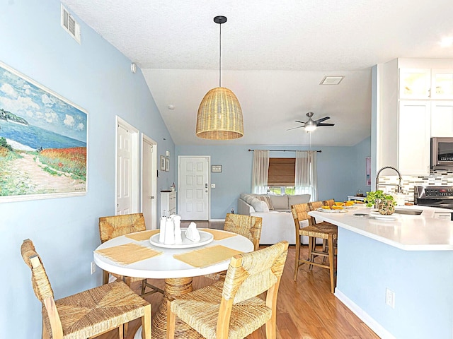 dining area featuring vaulted ceiling, light hardwood / wood-style flooring, sink, ceiling fan, and a textured ceiling