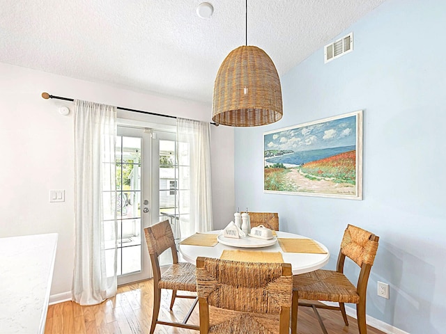 dining area with french doors, a textured ceiling, hardwood / wood-style floors, and vaulted ceiling