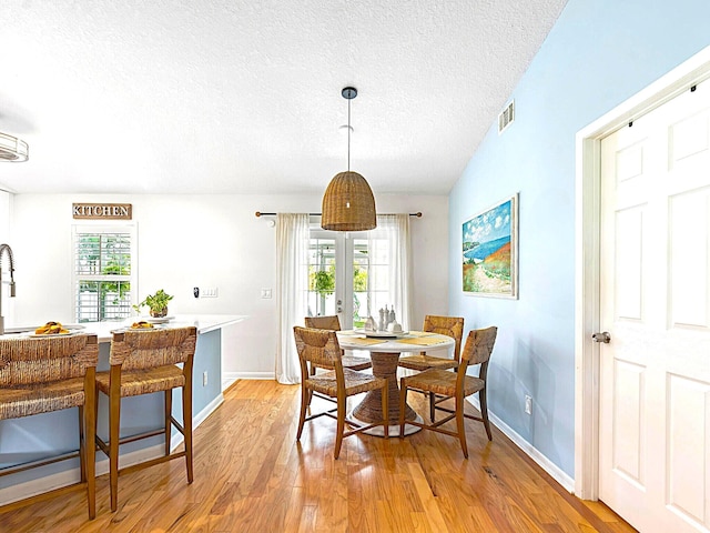 dining area with light wood-type flooring, a textured ceiling, and a healthy amount of sunlight