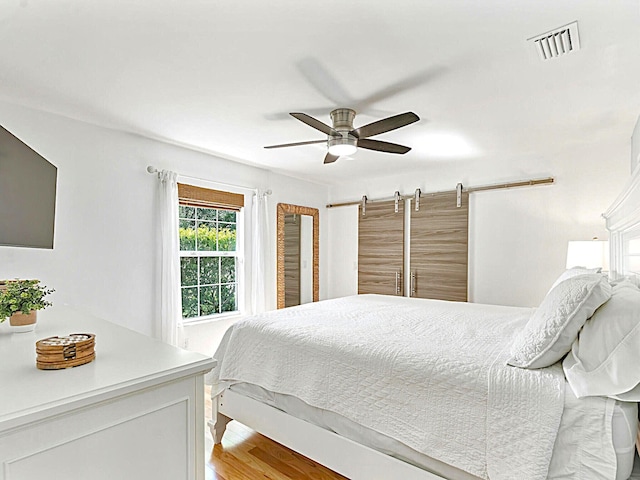 bedroom with light wood-type flooring, ceiling fan, and a barn door