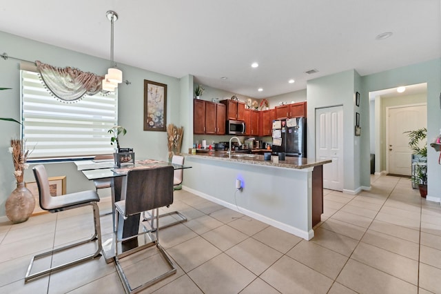 kitchen with light stone countertops, hanging light fixtures, black fridge, kitchen peninsula, and light tile patterned floors