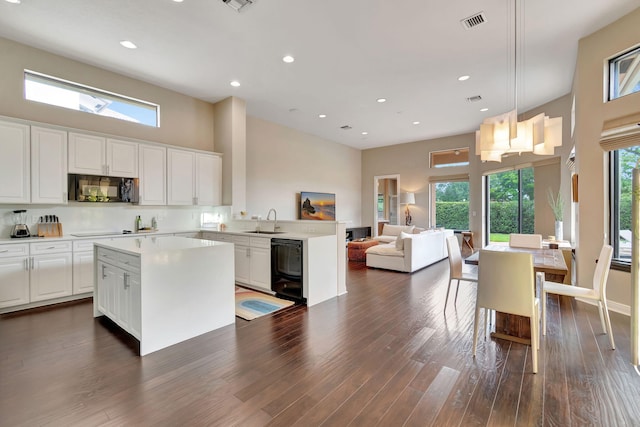 kitchen with black appliances, a kitchen island, dark hardwood / wood-style flooring, and white cabinetry