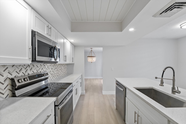 kitchen with decorative light fixtures, appliances with stainless steel finishes, sink, light wood-type flooring, and white cabinets