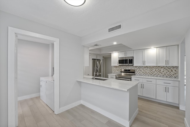 kitchen featuring washer and dryer, stainless steel appliances, white cabinets, and light hardwood / wood-style floors