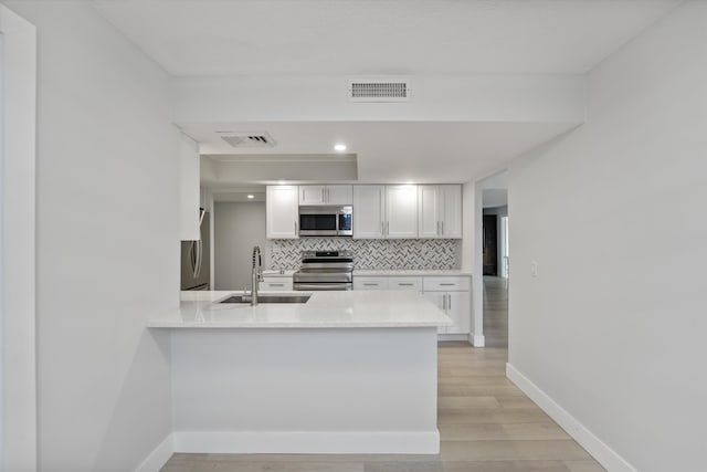 kitchen featuring white cabinets, light hardwood / wood-style flooring, appliances with stainless steel finishes, sink, and tasteful backsplash