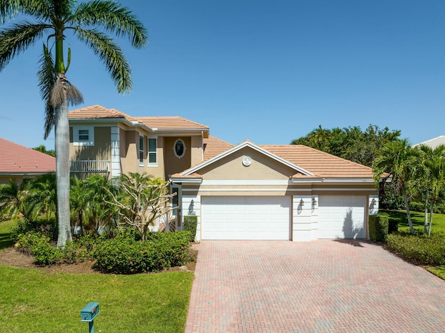 mediterranean / spanish-style house with an attached garage, a front yard, decorative driveway, and stucco siding