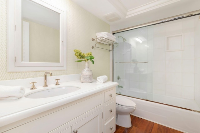 full bathroom featuring shower / bath combination with glass door, vanity, hardwood / wood-style flooring, crown molding, and toilet