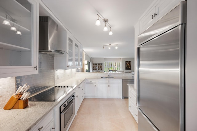 kitchen featuring sink, wall chimney range hood, appliances with stainless steel finishes, and white cabinetry