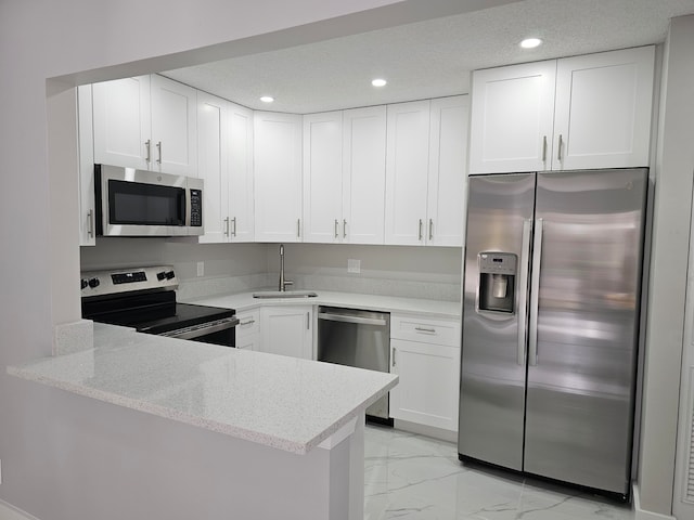 kitchen featuring light stone countertops, stainless steel appliances, white cabinetry, sink, and kitchen peninsula