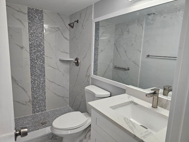 bathroom with toilet, a tile shower, and vanity