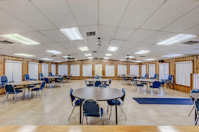 interior space featuring a paneled ceiling, ceiling fan, and wood walls