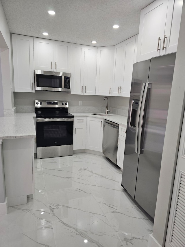 kitchen with appliances with stainless steel finishes, white cabinetry, sink, and a textured ceiling