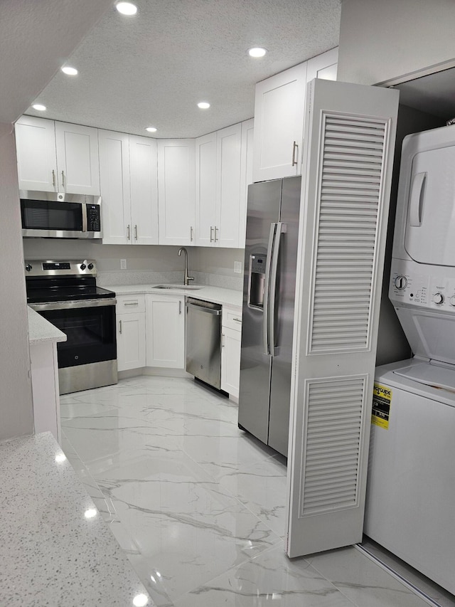 kitchen featuring appliances with stainless steel finishes, stacked washer / drying machine, and white cabinets