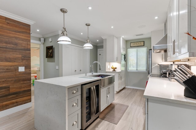 kitchen featuring wine cooler, decorative light fixtures, an island with sink, sink, and white cabinets