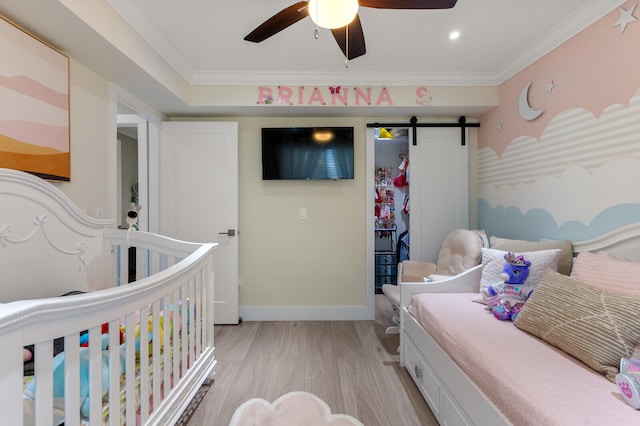 bedroom featuring light hardwood / wood-style flooring, ceiling fan, ornamental molding, a barn door, and a nursery area