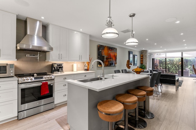 kitchen featuring ornamental molding, sink, stainless steel stove, wall chimney exhaust hood, and light hardwood / wood-style floors